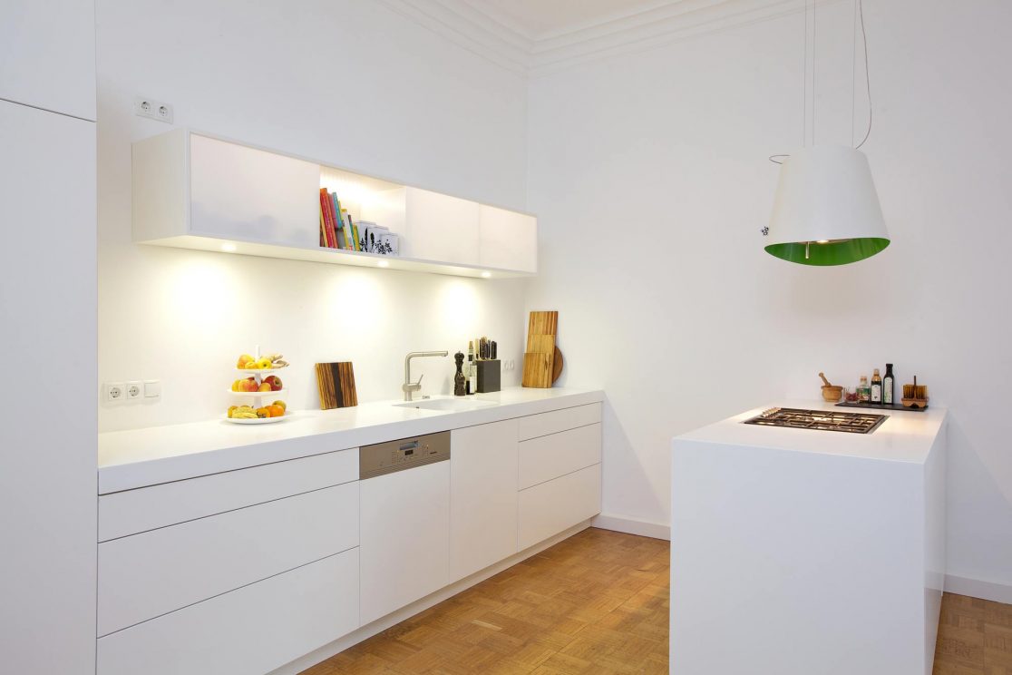 Weiße Küchenfront mit beleuchtetem Hängeregal und Kochfeld in Einzelelement